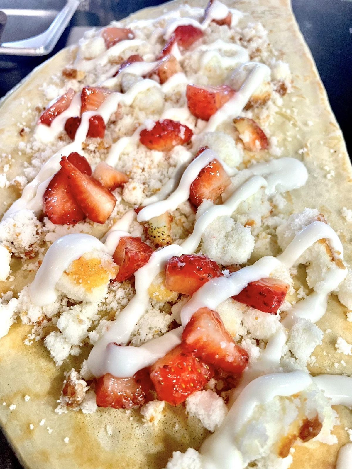 Sweet strawberry crepe with cream drizzle, fresh strawberries, and crumble topping